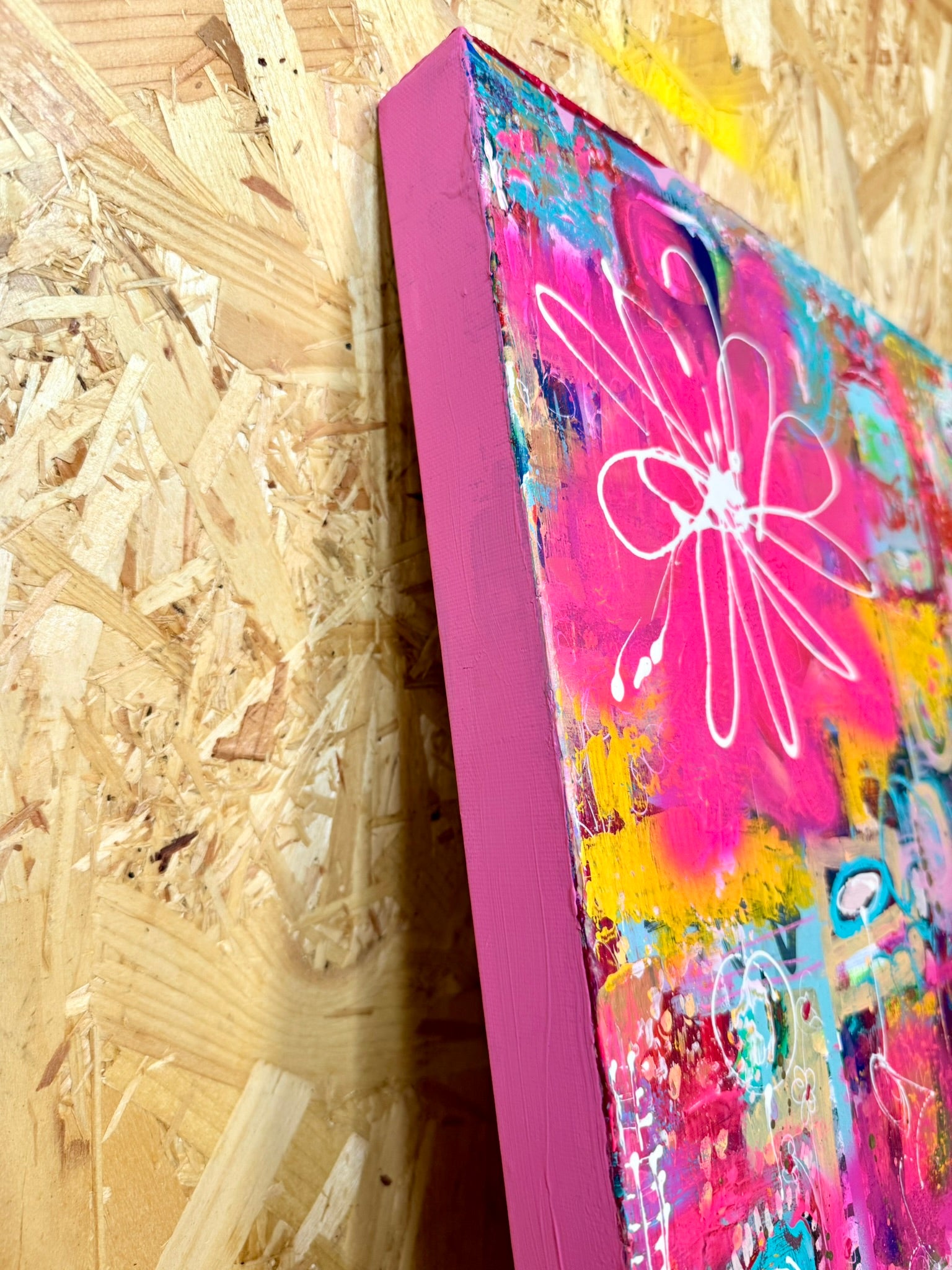 Colorful abstract painting with a pink frame on a wooden surface
