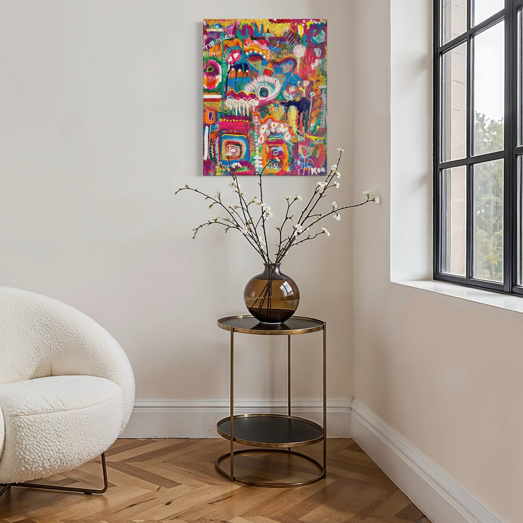 White armchair in a room with a colorful abstract painting on the wall and a small table with a vase and branches.