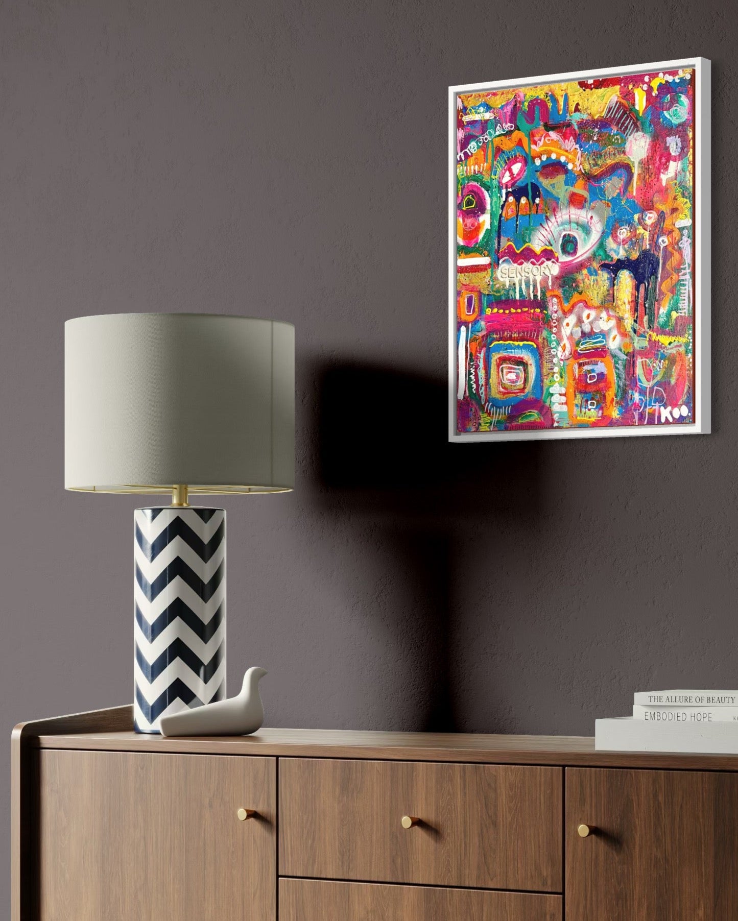 Wooden sideboard with a lamp and decorative items against a dark wall with a colorful abstract painting.